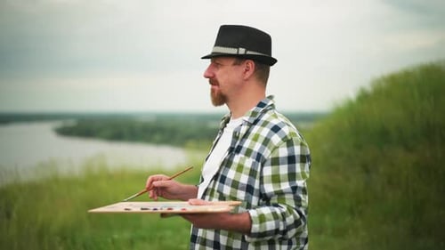 Artist Paints Outdoors in Grassy Field with River View