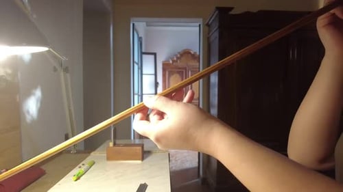 Female violin bow maker checking straightness of wooden bow stick in traditional luthier workshop