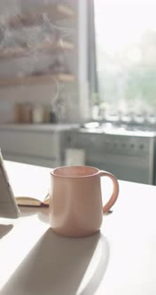 Vidéo verticale : tasse à café fumante sur le comptoir de la cuisine à côté d'une tablette dans une lumière matinale