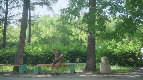Young Man Sitting on Bench in a Green Park