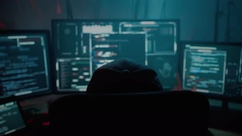 Hooded Figure Working with Multiple Computer Screens