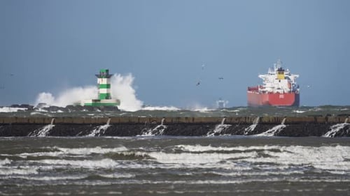 Coastal view of green and white lighthouse and big ship in stormy sea conditions