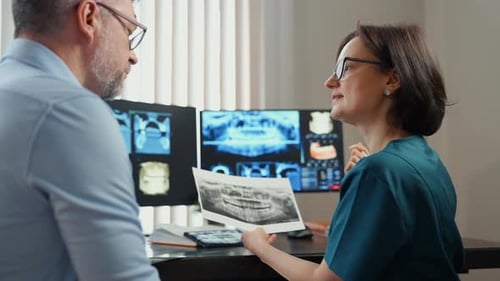 Close Up View of Dentist Consulting Patient While Reviewing Dental Xrays and Scans on Monitor Modern