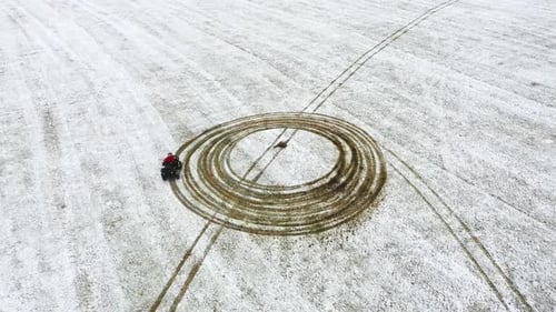 The adult person on an ATV in a snow-filled farm field - Aerial view