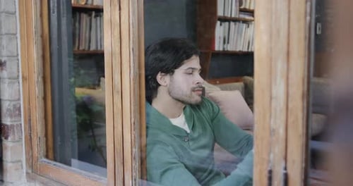 Happy caucasian man using smartphone sitting by window at home, slow motion
