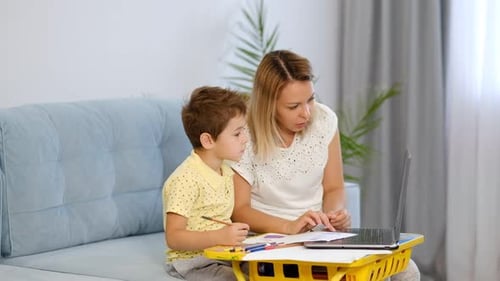Young Mother or Nanny Helps a Little Boy Complete an Assignment in an Online School