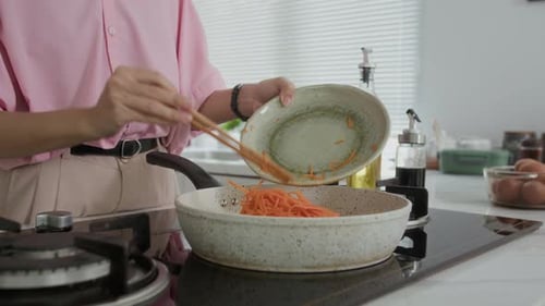 Woman Cooking Carrots in Kitchen with Chopsticks
