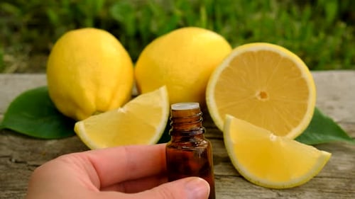 Hand Holding Lemon Oil Bottle With Ripe Fruit