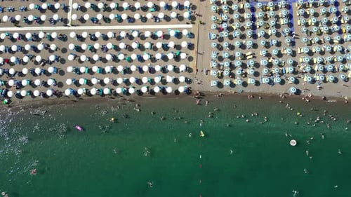 A drone flies over a beautiful beach with umbrellas. People sunbathe and swim in the transparent sea