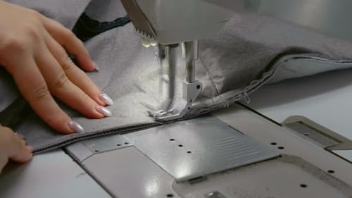 Close-up view of woman hands working sewing machine stitching fabric.