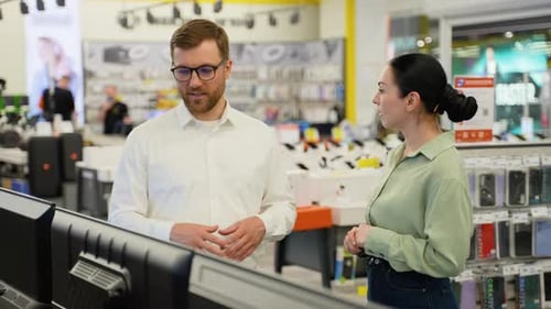 Salesman Helping Young Woman Choosing New Tv in Electronics Store