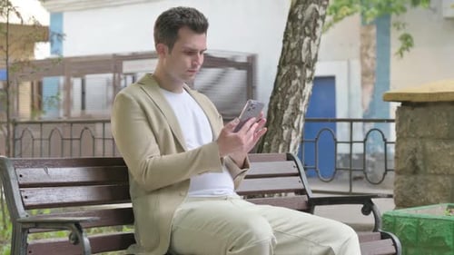Young Adult Using Mobile Phone on Park Bench