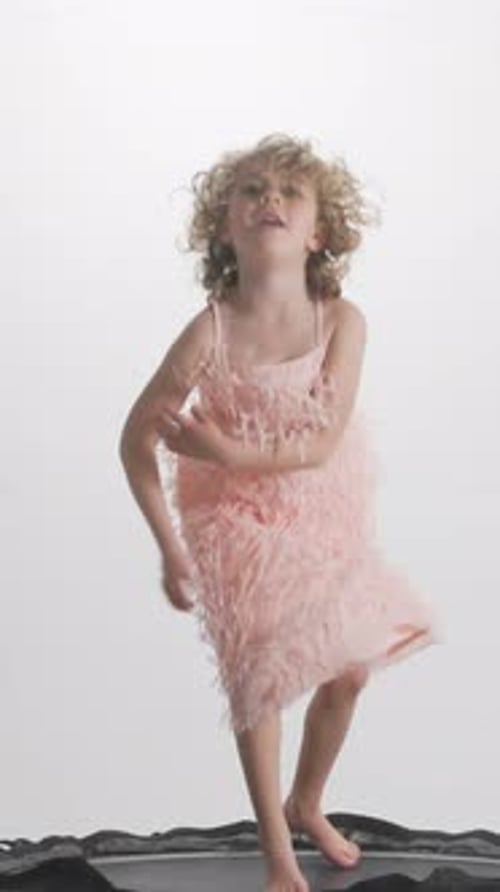 Excited Girl Jumping on Trampoline in Pink Dress