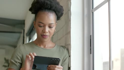 Woman Uses Cellphone Indoors by a Bright Window