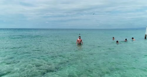 Young Caucasian strong athletic man wearing bathing suit walking in clear ocean water on cloudy day,
