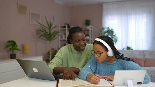 Supportive black mother helping her teenage daughter with her school homework at home