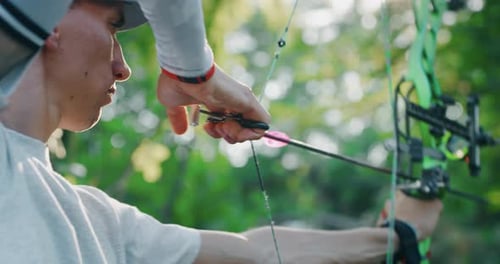 Slow motion close up of young man with professional equipment is practising archery with a bow in