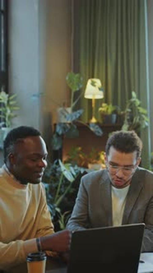 Two Young Men Talking about Business Presentation on Laptop in Office