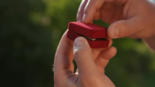 Nahaufnahme einer Samtschachtel mit einem Ring darin, die von einem Mann mit seinen Händen geöffnet wird
