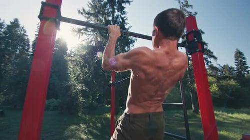 Pull ups in the park. Young caucasian man with lean body works out in the park and performs exercise
