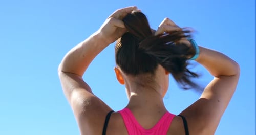 Woman Puts Hair into Ponytail Outside on Sunny Day