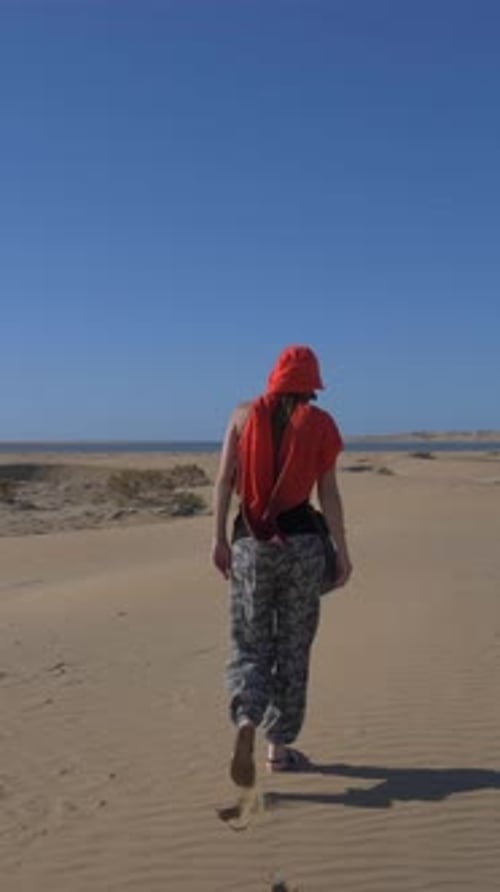 Mature woman wearing a red turban walking on the sand dunes of the Sahara desert under a blue sky