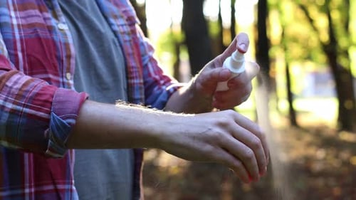 Man spraying tick repellent onto arm in park, closeup. Camera moving