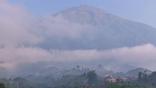 Scenic shot of lush hills and terraced farms beneath a mist-shrouded tropical mountain