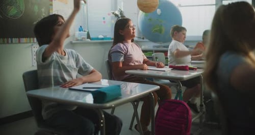 Elementary School Students Sitting at the Desks Raising Hands to Provide Correct Answer