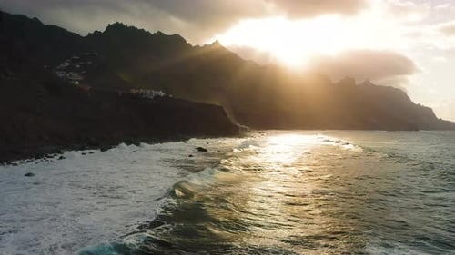 Ocean Waves Foaming Roll on the Rocky Shore with Mountain Range in Sunset Light Tenerife Canary