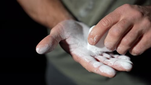 Strong male sportsman applying magnesium carbonate chalk dust to hands, Close up shot