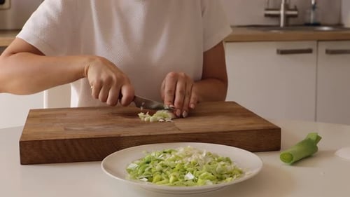 Woman Cuts Fresh Leek on Cutting Board in Kitchen