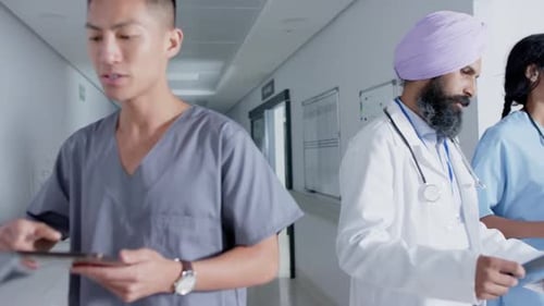 Diverse doctors and nurses using tablets and walking through corridor at hospital, in slow motion