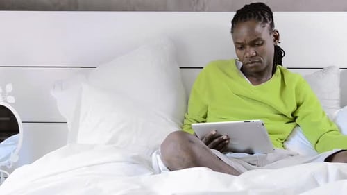 Man with Dreadlocks Relaxing on Bed with Tablet
