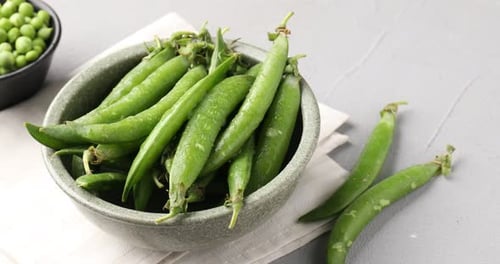 Fresh ripe green peas on grey table, closeup. Camera moving left