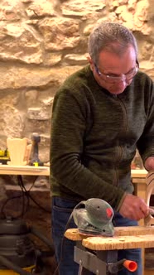 Carpenter using an electric tool to polish a piece of wood in studio workshop