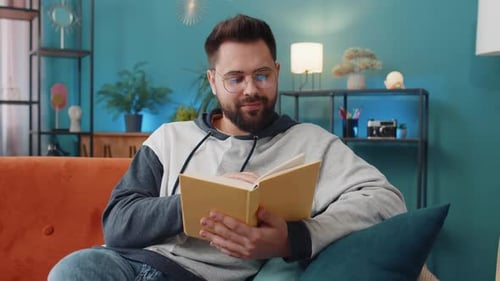 Young Man Relaxing Interesting Book Turning Pages Smiling Enjoying Literature Taking a Rest on Sofa
