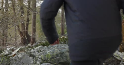 man in black pants and hiking boots walks through forest and jumps onto rock