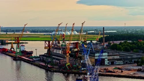 Luftaufnahme eines Industriegebiets am Flussufer mit mehreren hohen Ladekranen, angedockten Schiffen,