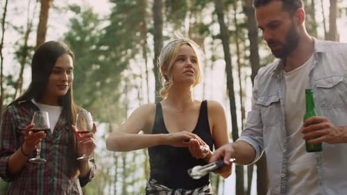 Smiling blonde woman salting bbq meal with friends in summer forest outdoors