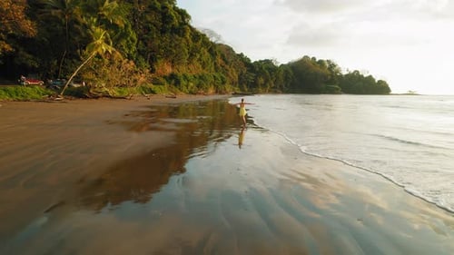 Happy woman running through waves at Dominicalito Beach in sunset Costa Rica