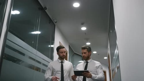 Business Team Walking Together Talking Corporate Project Plan Using Tablet Device In Office. Two ...