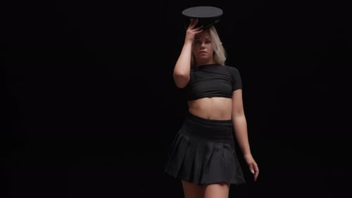 Young Woman in Policemans Hat Dances in Studio Against Black Background