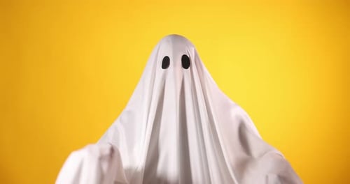 Creepy ghost. Man covered with white sheet showing scary moves on orange background