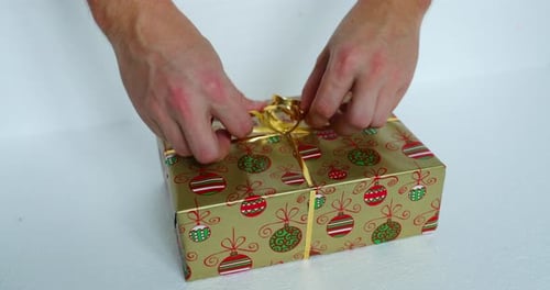 Hands Tie Bow on Gold Christmas Gift