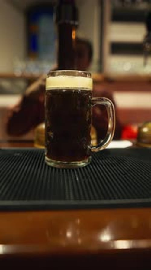 A Dark Beer is Displayed in a Mug on a Bar Counter While the Bartender Prepares a Drink