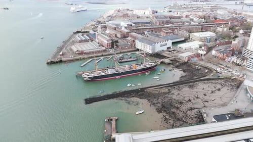 Dropping drone footage of HMS Warrior in Portsmouth Docks with Naval Base beyond and busy harbour wi