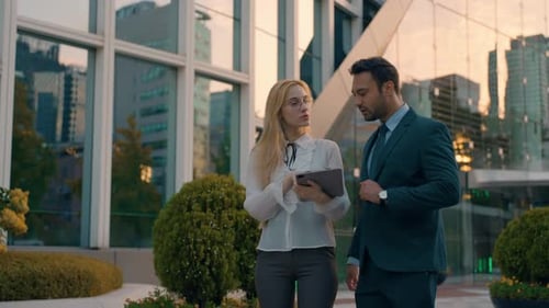 Two young successful Architects male and female business people outside big office building at sunse