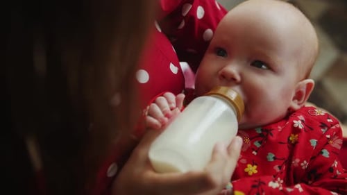 Infant Drinking Milk from Bottle Held by Adult