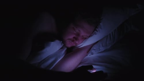 Schlafloser Mann, der an Schlaflosigkeit leidet, wacht mitten in der Nacht auf, um auf sein Smartphone zu schauen
